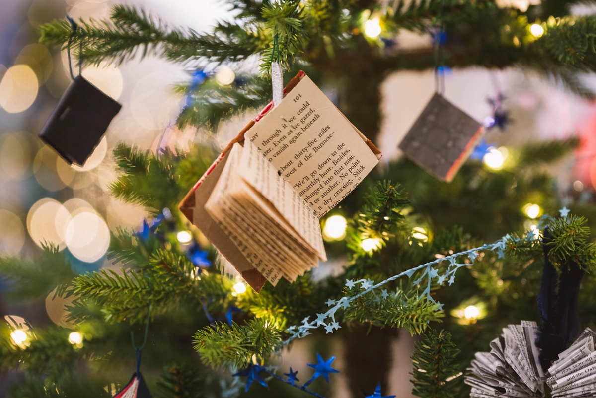 Un albero di Natale decorato con mini-libri aperti come ornamenti, lucine dorate e stelline blu in un&#039;atmosfera festiva con luci sfocate. 