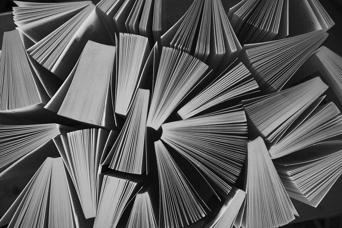 Foto in bianco e nero di numerosi libri aperti a ventaglio, disposti a formare una composizione circolare. 