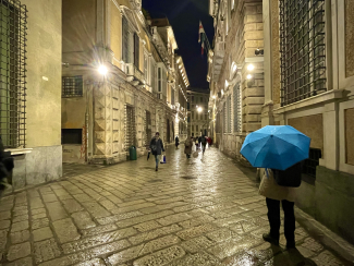 Persona con ombrello blu che passeggia in via Garibaldi in una serata di pioggia 