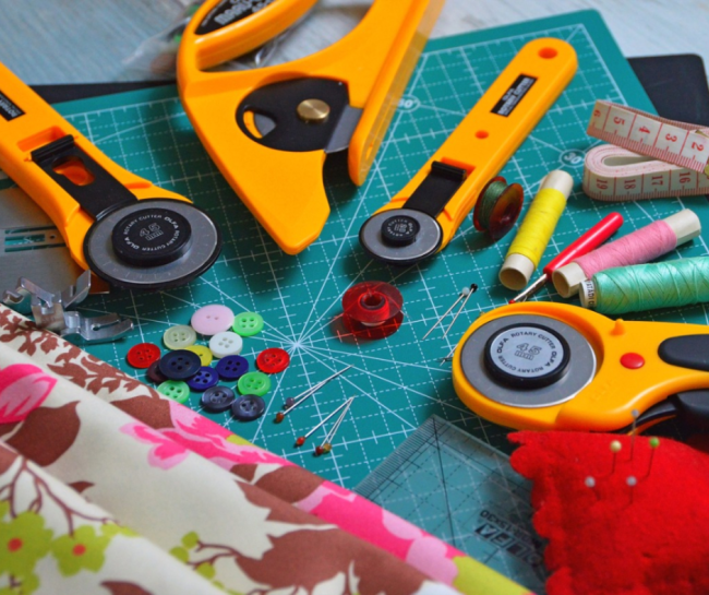 Strumenti e materiali per cucito su tappetino da taglio: taglierini rotativi, bottoni, filo e tessuto