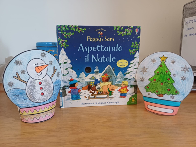 Libro per bambini "Poppy e Sam Aspettando il Natale" esposto centralmente tra due decorazioni artigianali a forma di palla di neve natalizia.