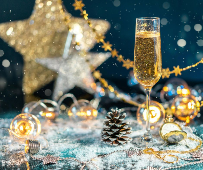 Un calice di spumante frizzante circondato da decorazioni natalizie dorate e argentate con luci sfocate e atmosfera festiva.