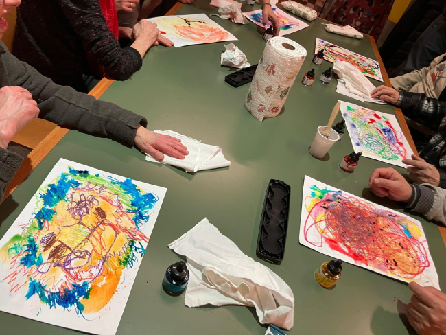 Un gruppo di persone attorno a un tavolo crea disegni astratti e colorati usando colori e inchiostri.