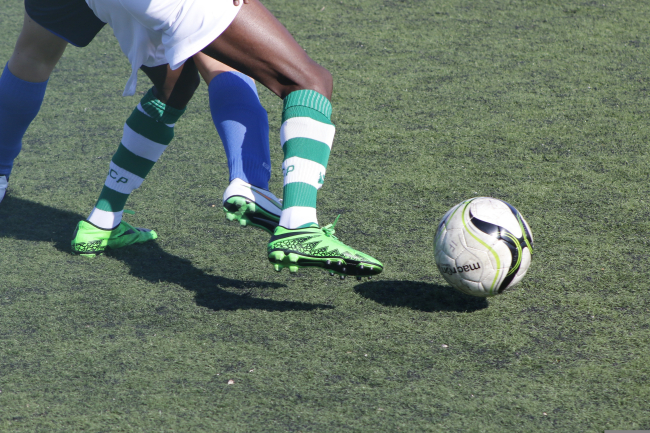 Primo piano su un campo in erba sintetica: le gambe di due calciatori in contrasto,