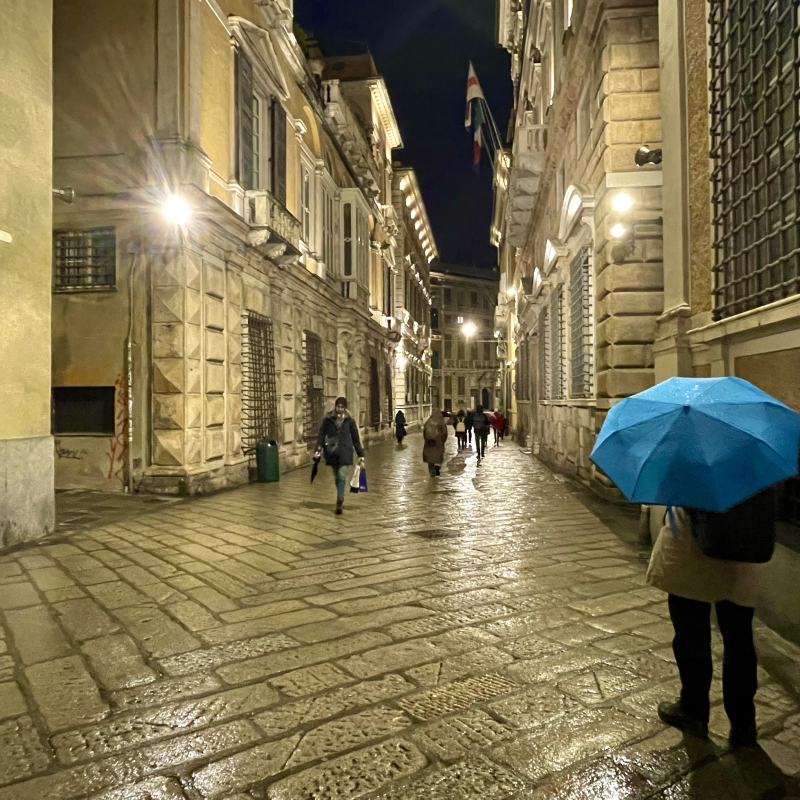 Persona con ombrello blu che passeggia in via Garibaldi in una serata di pioggia